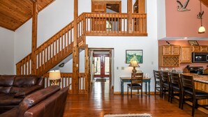 A spacious living area with a wooden staircase, a dining area with wooden chairs and a table, and a kitchen with wooden cabinets. - Slip Away Chalet 4 Bedroom House (McHenry)