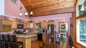A spacious kitchen with wooden cabinets, a large island, and a dining area with a wooden table and chairs. - Slip Away Chalet 4 Bedroom House (McHenry)