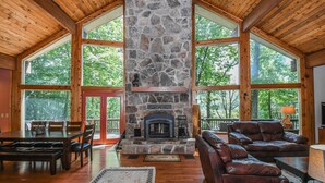 A spacious room with a stone fireplace, wooden ceiling, large windows, and a leather sofa. - Slip Away Chalet 4 Bedroom House (McHenry)