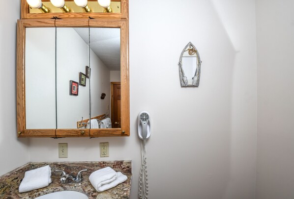 Un baño con un espejo de marco de madera, un secador de pelo y un perchero para toallas.