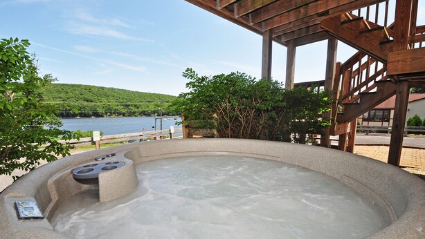 Un jacuzzi con una pérgola de madera arriba, rodeado de follaje y vistas a un lago.
