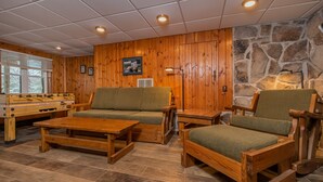 A cozy room with wooden walls, a stone accent wall, a green sofa, a wooden coffee table, and a wooden armchair. - Ski Shore 3 Bedroom House (Swanton)
