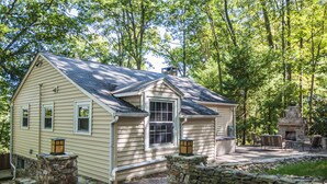 A small, single-story house with a stone chimney, a stone wall, and a patio with outdoor furniture. - Ski Shore 3 Bedroom House (Swanton)
