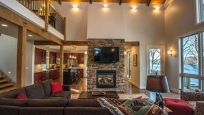 A spacious living area with a stone fireplace, a large flat-screen TV mounted above it, and a cozy seating arrangement.