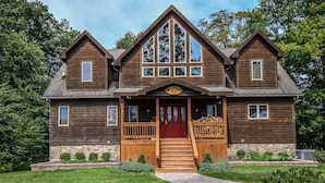 A two-story wooden house with a red front door, a wooden porch, and a stone foundation. - Midnight Dip 6 Bedroom House (Swanton)