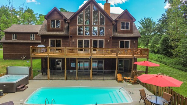 A large two-story house with a swimming pool, deck chairs, and umbrellas. - Midnight Dip 6 Bedroom House (Swanton)