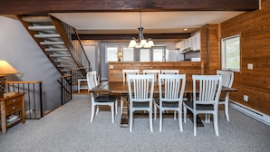 A dining area with a wooden table and chairs, a staircase, and a kitchen in the background.