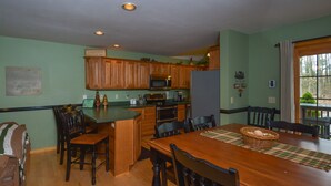 A kitchen with wooden cabinets, a microwave, and a refrigerator. There is a dining table with chairs and a placemat.