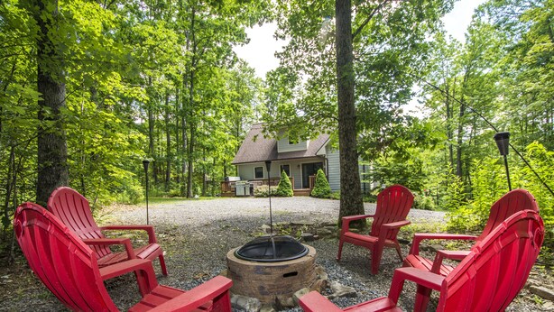 A wooden deck with four red Adirondack chairs arranged around a central fire pit.
