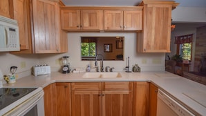 A kitchen with wooden cabinets, a white countertop, a sink, a toaster, a blender, and a dishwasher. - All About Me 4 Bedroom House (McHenry)