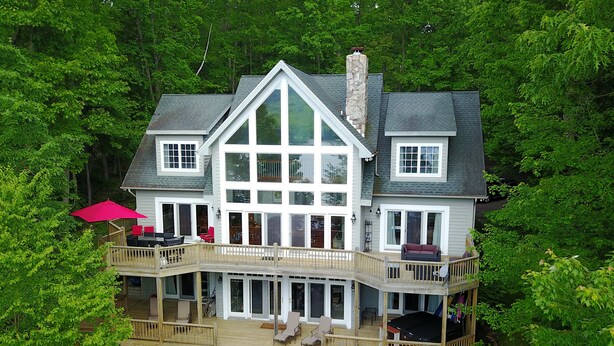 A large, two-story house with a balcony and deck, surrounded by dense greenery. - Friday's Escape 7 Bedroom House (McHenry)