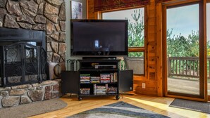 A living room with a stone fireplace, a flat-screen TV on a stand, and a bookshelf.