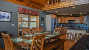 A spacious dining area with a wooden table and chairs, a kitchen with wooden cabinets, and a staircase leading to an upper level.