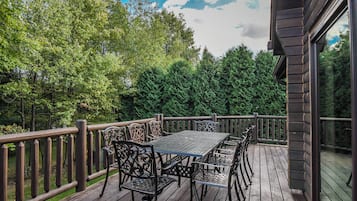 An outdoor deck with a table and chairs, surrounded by a wooden railing and dense trees.