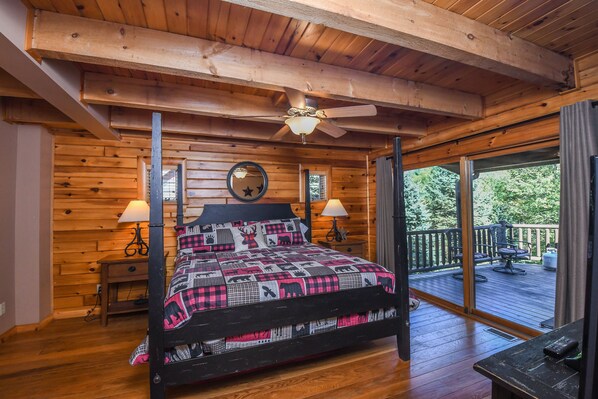 A wooden cabin bedroom with a four-poster bed, a ceiling fan, and a view of the deck.