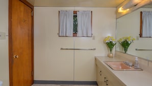 A bathroom with a wooden door, a window with curtains, a sink with a mirror, and two vases with flowers. - Simpson's Sanctuary 3 Bedroom House (McHenry)