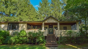 A log cabin with a front porch, a staircase leading to the entrance, and a surrounding forest. - Simpson's Sanctuary 3 Bedroom House (McHenry)