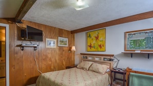 A bedroom with a wooden ceiling, a bed with a floral bedspread, a mounted TV, and artwork on the walls. - Simpson's Sanctuary 3 Bedroom House (McHenry)