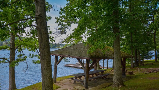 A lakeside picnic area with a wooden gazebo, benches, and a dock in the background. - Simpson's Sanctuary 3 Bedroom House (McHenry)