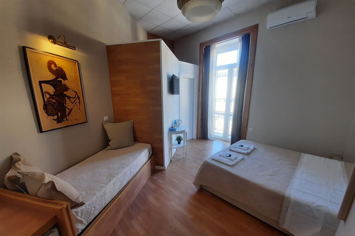 A hotel room with two single beds, a wooden partition wall, a mounted TV, and a window with curtains.