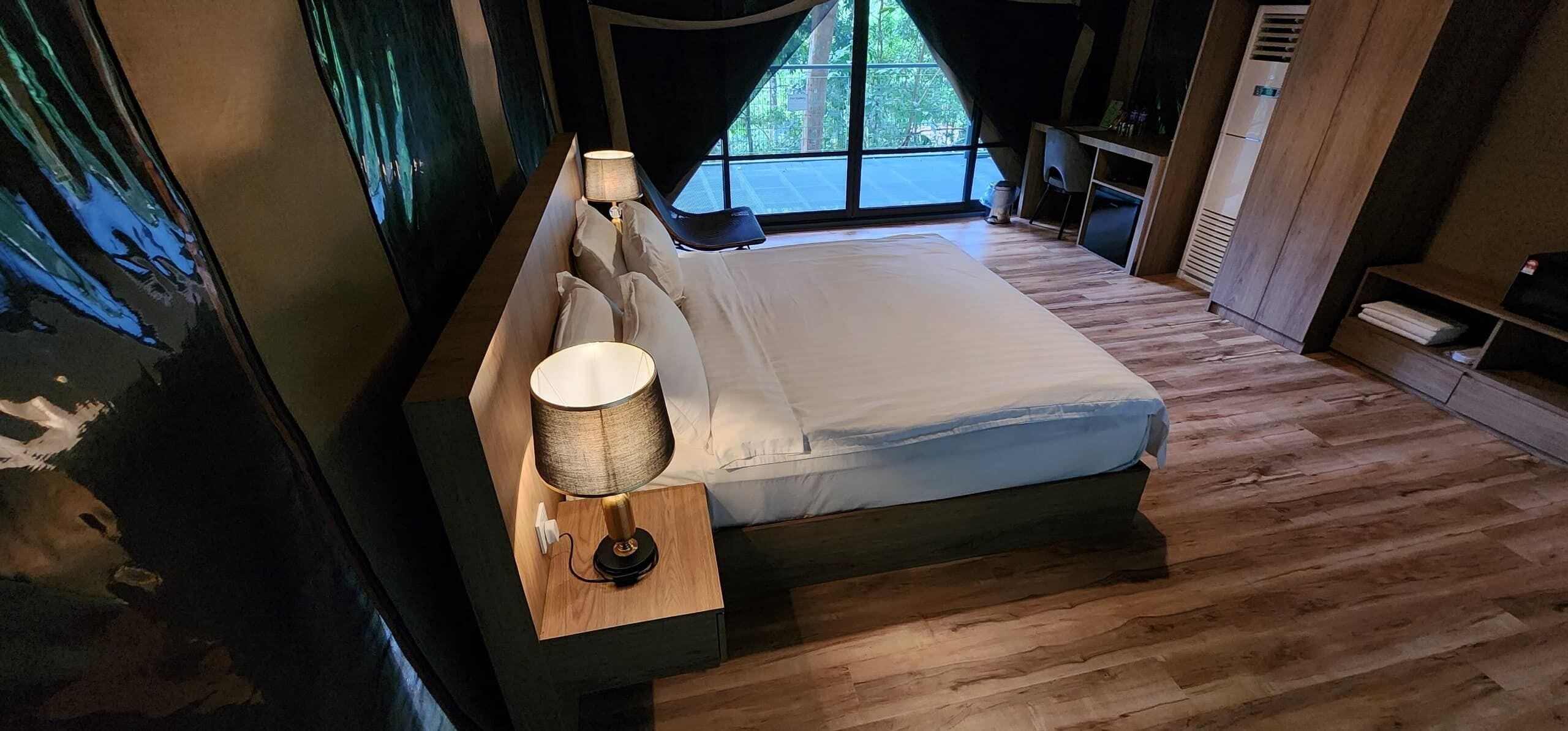 Ein Schlafzimmer mit einem großen Bett, einer Nachttischlampe und Blick ins Freie durch ein Fenster.