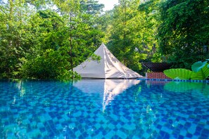 A swimming pool with a tent structure in the middle, surrounded by lush greenery.
