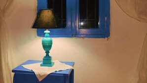 Une pièce avec une fenêtre bleue, une petite table bleue sur laquelle se trouve une lampe, et des rideaux blancs.