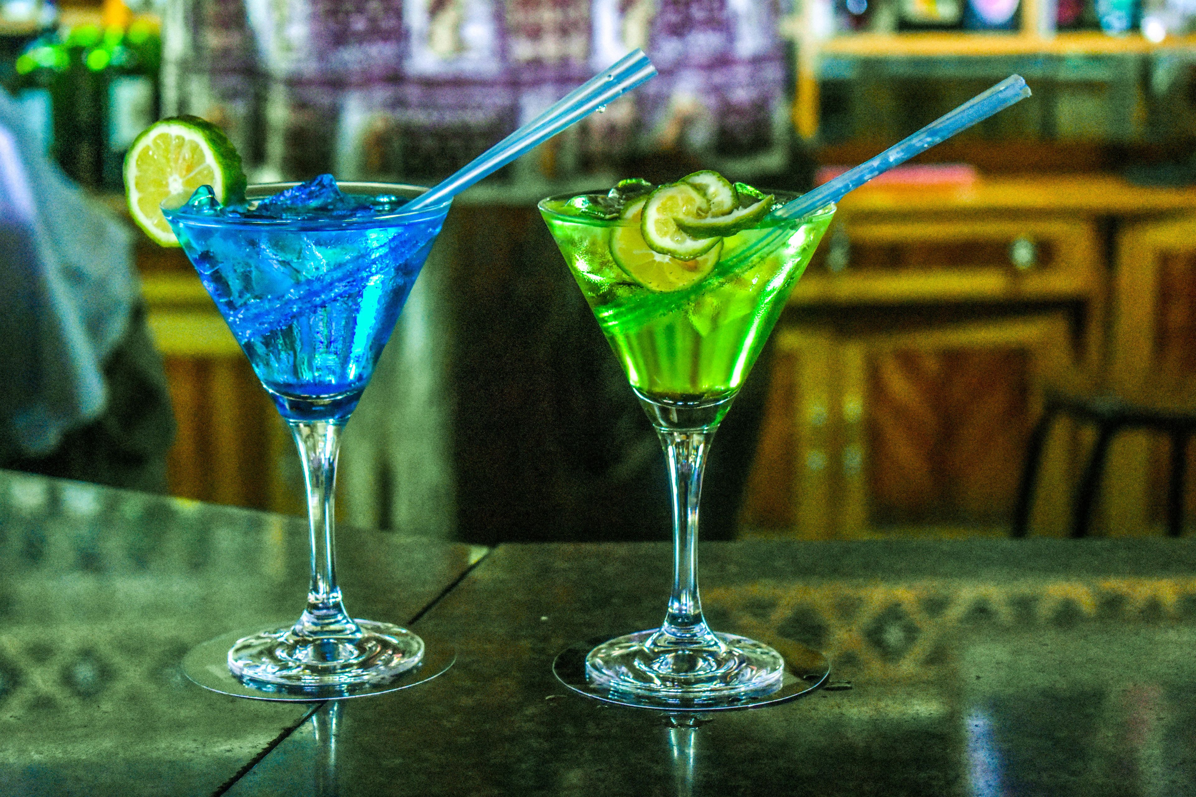 Two cocktails on a bar counter with a blurred background.
