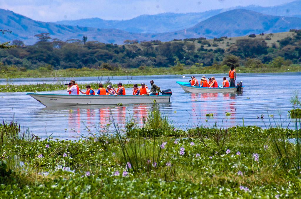 Two boats on a calm lake with people wearing life jackets, surrounded by lush greenery and hills in the background.