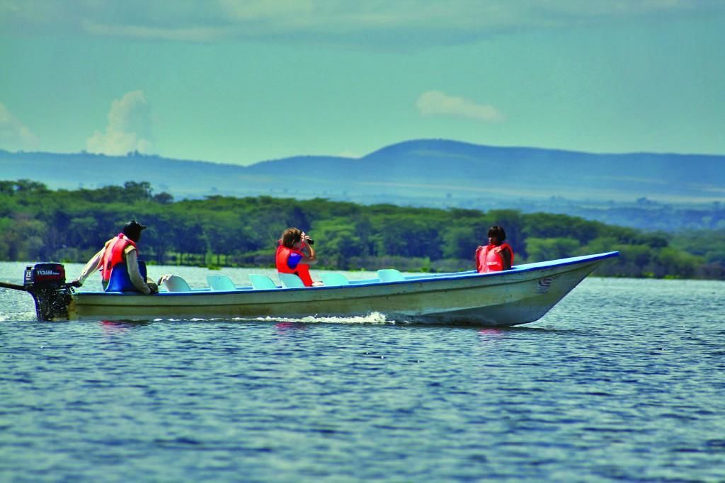 Un petit bateau avec deux personnes à bord, sur un lac paisible, entouré de verdure et de collines lointaines.