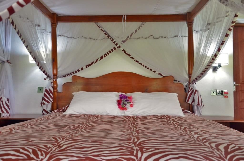 Una cama con dosel con dosel, ropa de cama con estampado de cebra, cabecera de madera y cortinas a rayas.