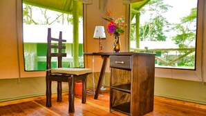 Una habitación con una silla de madera, una pequeña mesa con una lámpara y un florero con flores.