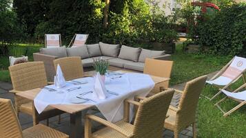 An outdoor dining area with wicker furniture and a round table set for a meal.