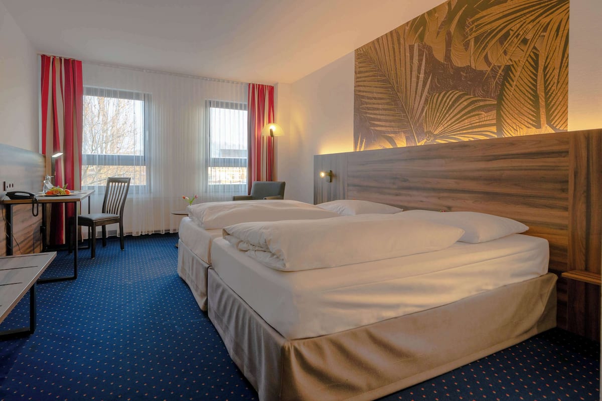 A hotel room with a large bed, a desk, a chair, and a window with curtains.