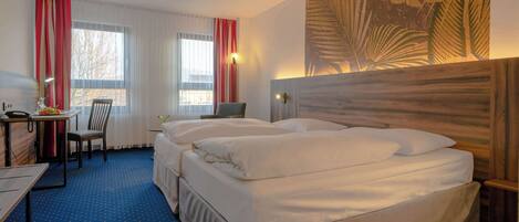 Una habitación de hotel con una cama grande, un escritorio, una silla y un ventanal con cortinas.