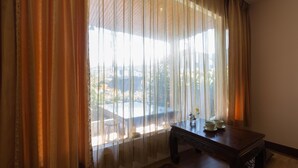 Huoneessa on suuri ikkuna, joka on peitetty läpikuultavilla verhoilla. Siellä on myös puinen pöytä, jossa on maljakko ja teekuppeja, sekä kuviollinen matto lattialla.