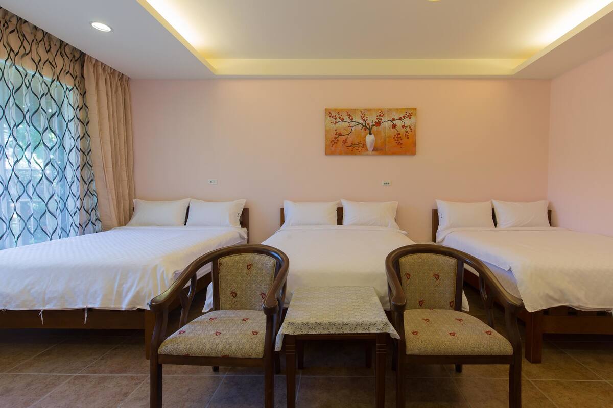 A hotel room with three beds, a table, and two chairs.