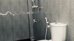 Un baño moderno con inodoro blanco, ducha con cabezal de ducha manual y grifo empotrado.
