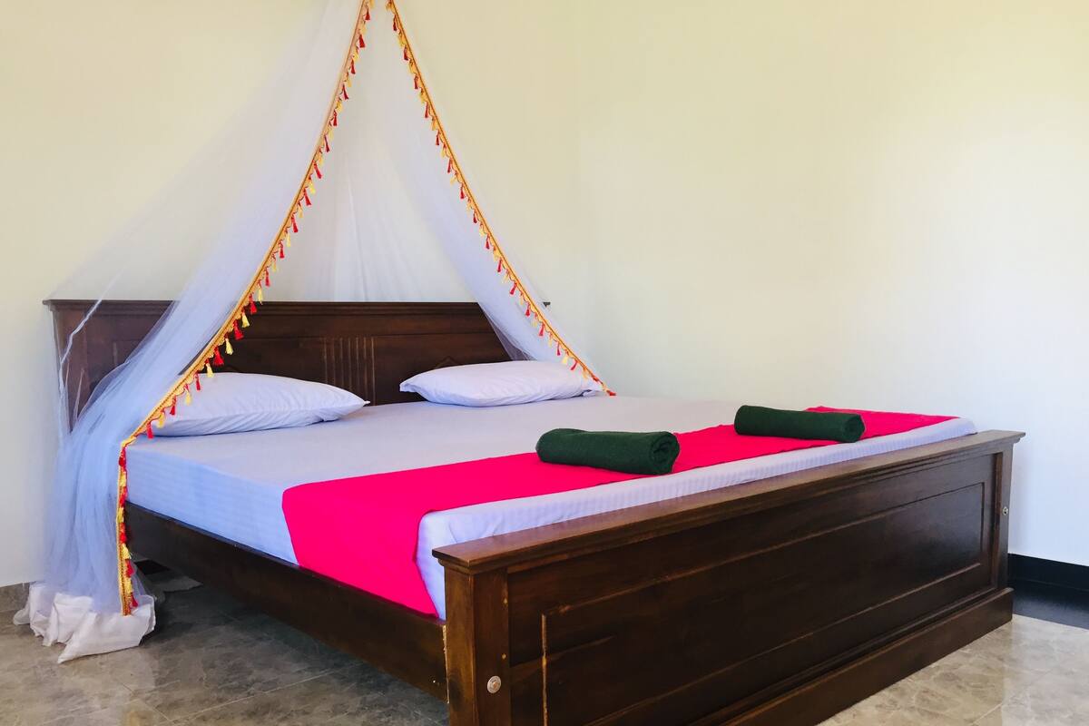 Una cama con cabecera de madera, ropa de cama blanca, una manta roja y dos toallas verdes.