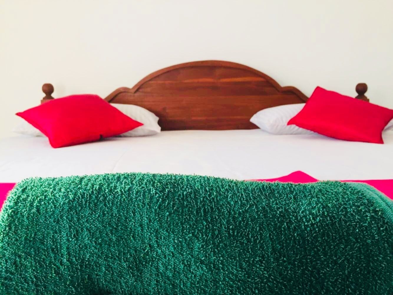 A bed with a wooden headboard, two red pillows, and a green textured blanket.