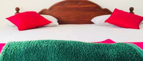A bed with a wooden headboard, two red pillows, and a green textured blanket.