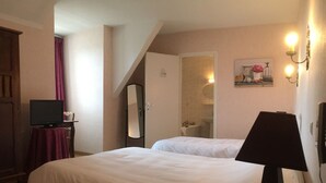 A bedroom with a bed, a desk with a lamp, a mirror, and a bathroom visible through an open door. - Mimat'hôtel (Mende)