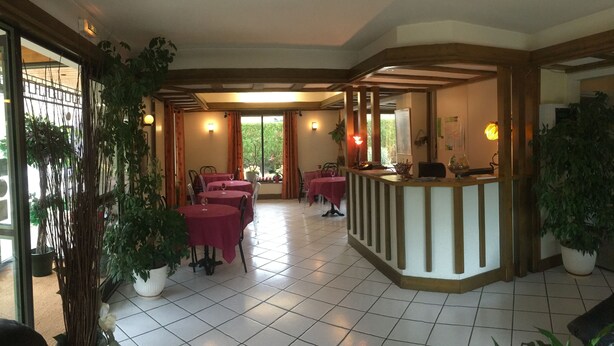 A hotel lobby with a reception desk, several tables with red tablecloths, and potted plants. - Mimat'hôtel (Mende)
