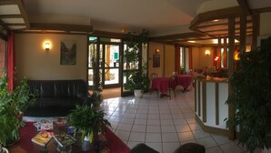 A hotel lobby with a leather sofa, dining area, and potted plants. - Mimat'hôtel (Mende)