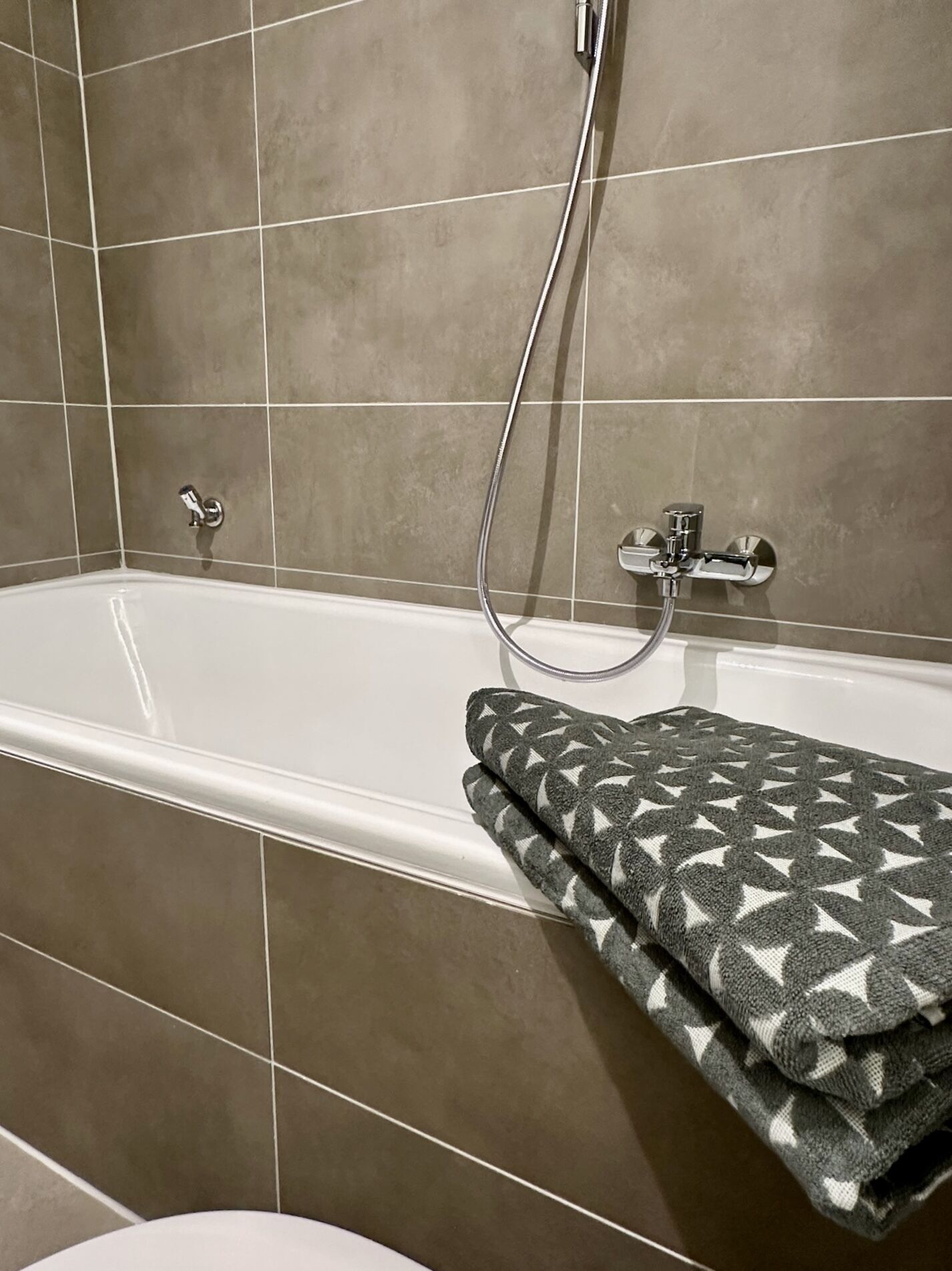 Ein Badezimmer mit einer weißen Badewanne, einer Duschbrause und einem Handtuch mit geometrischem Muster.