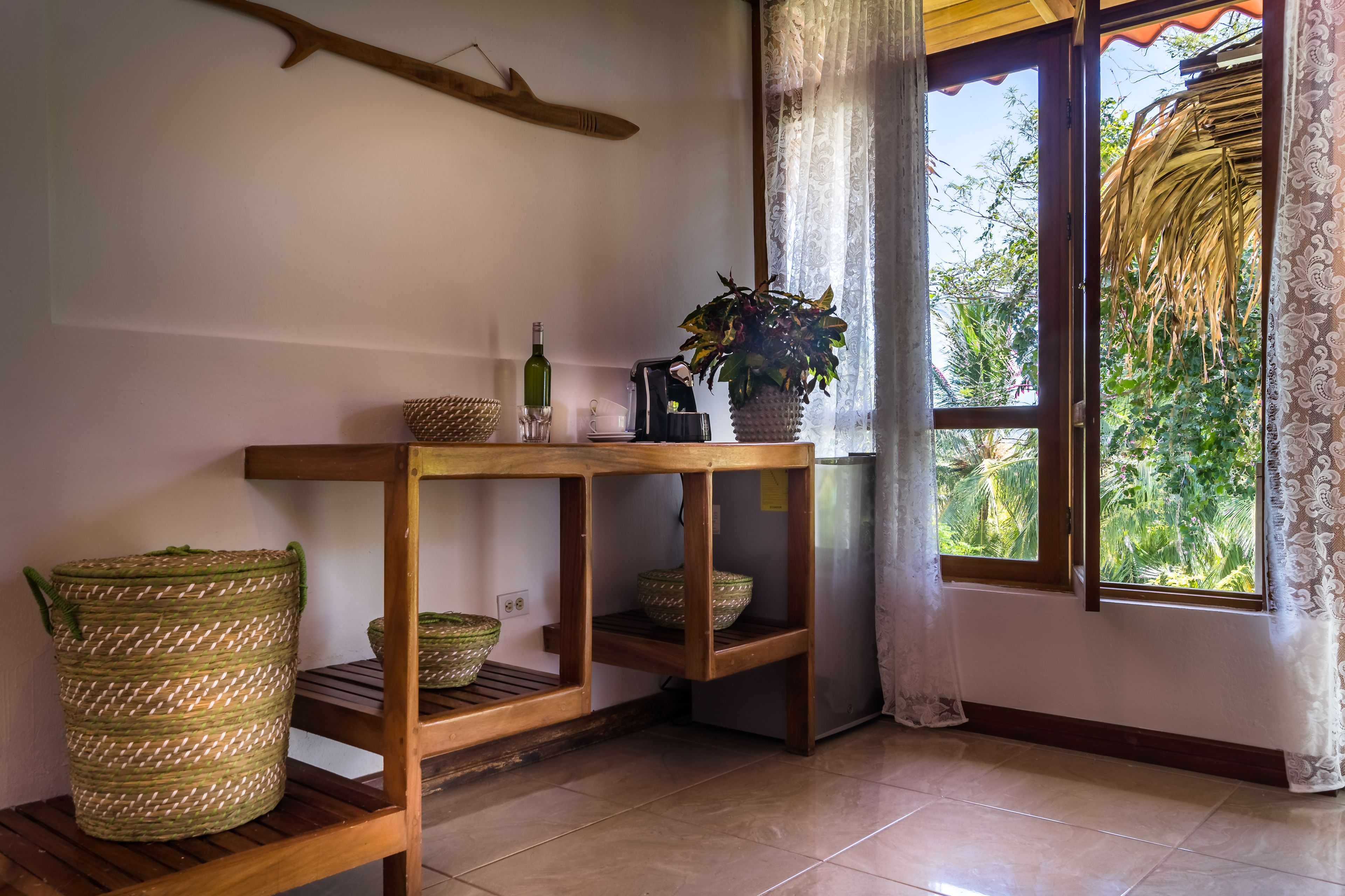A wooden table with woven baskets and a potted plant, a bottle, and a coffee maker.