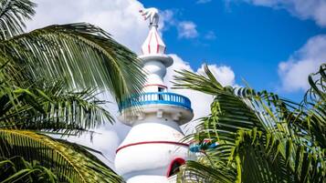 A white tower with red and blue stripes and a statue on top, surrounded by palm trees.