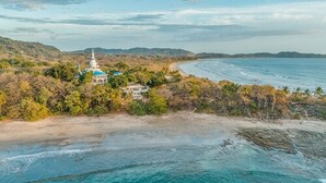 A coastal view with a pagoda-style building surrounded by lush greenery and a beach. - Nosara Beach Hotel (Nosara)