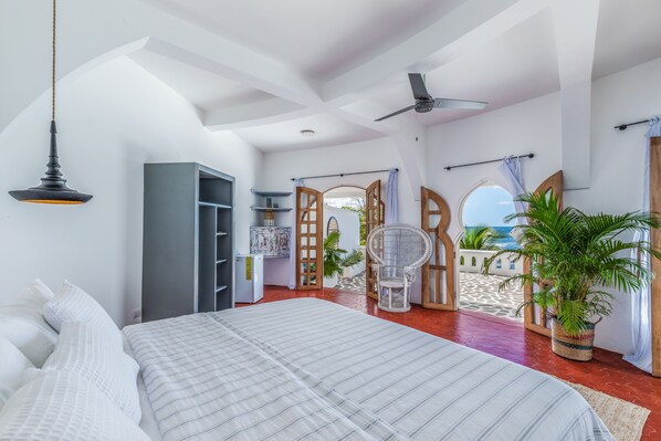A bedroom with a bed, a ceiling fan, a window, and a view of the beach. - Nosara Beach Hotel (Nosara)
