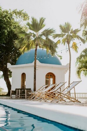 A poolside area with lounge chairs, a small building with a blue dome, and palm trees. - Nosara Beach Hotel (Nosara)